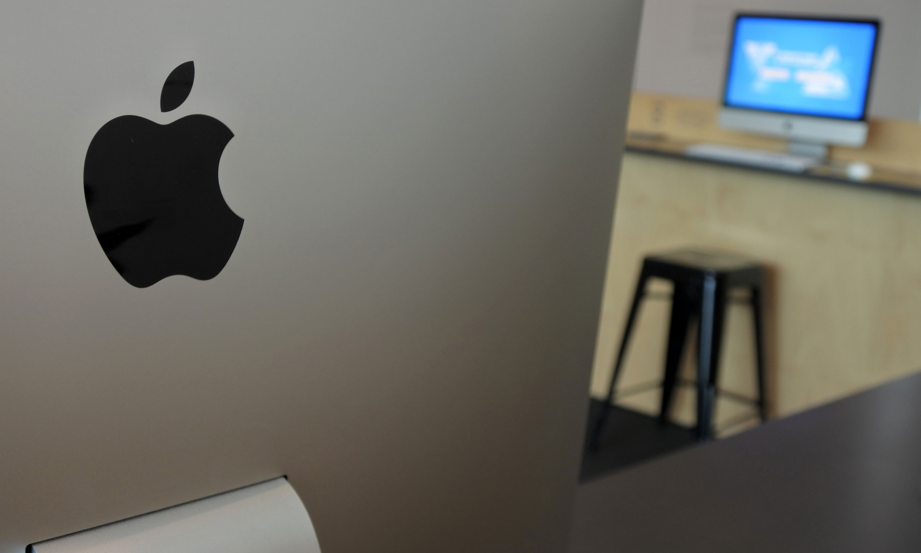 An Apple logo on a device with a computer monitor in the background.
