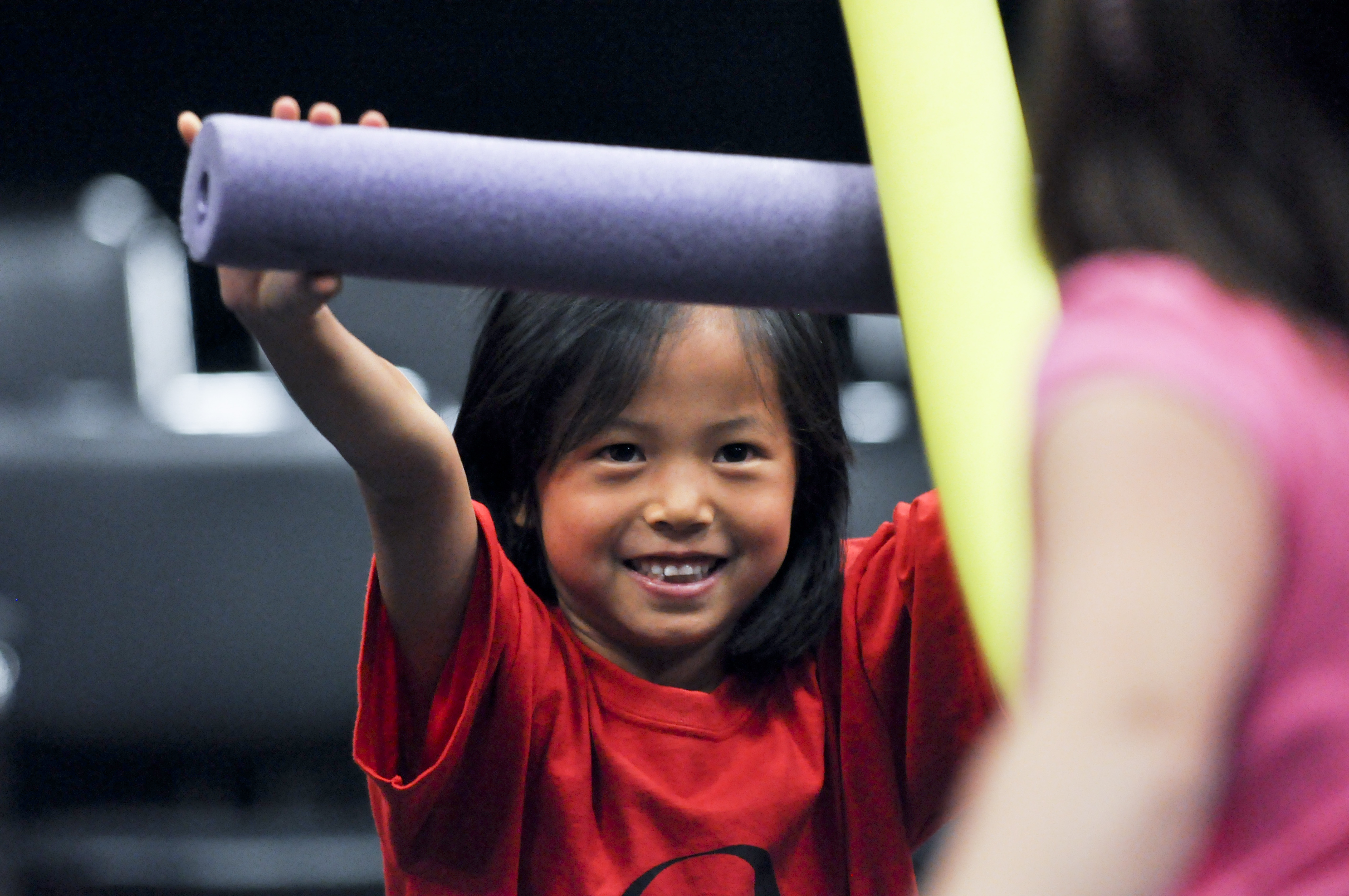 Young children sword fight with pool noodles