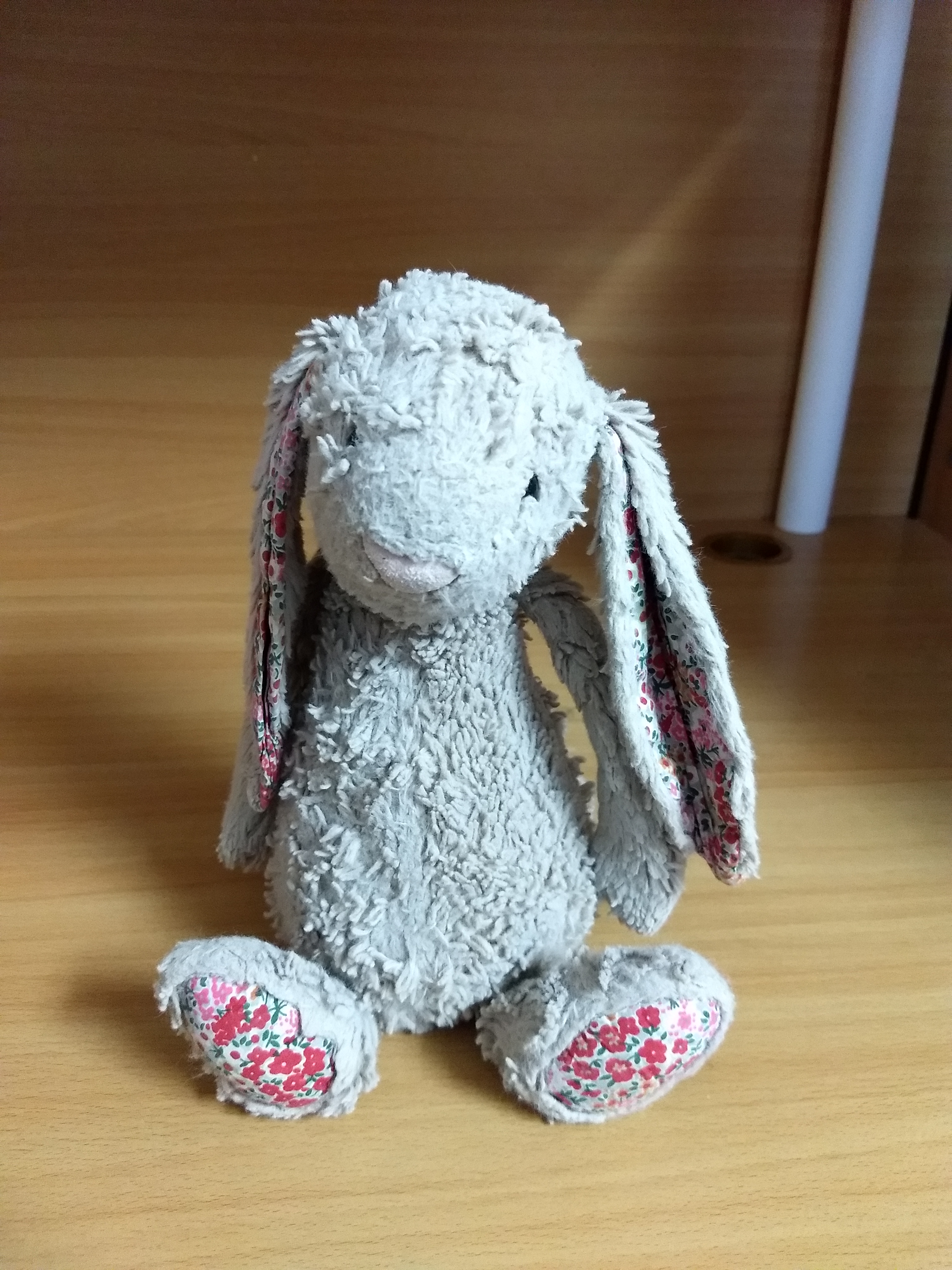 Photo of gray stuffed bunny with red, pink floral pattern on feet and ears