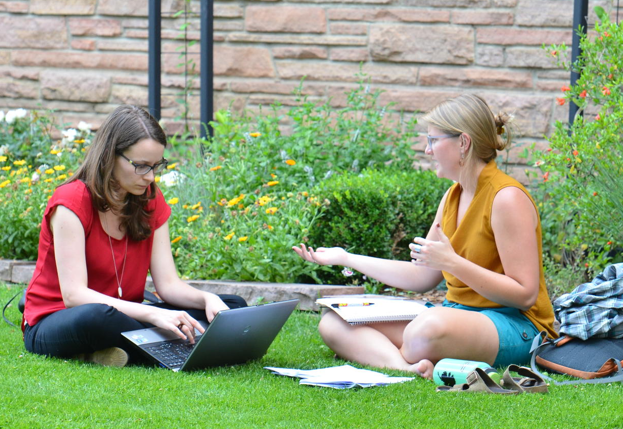 Graduate students sit on grass talking