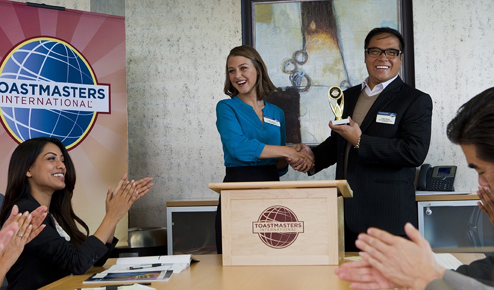 People shake hands, looking celebratory, at a lectern.