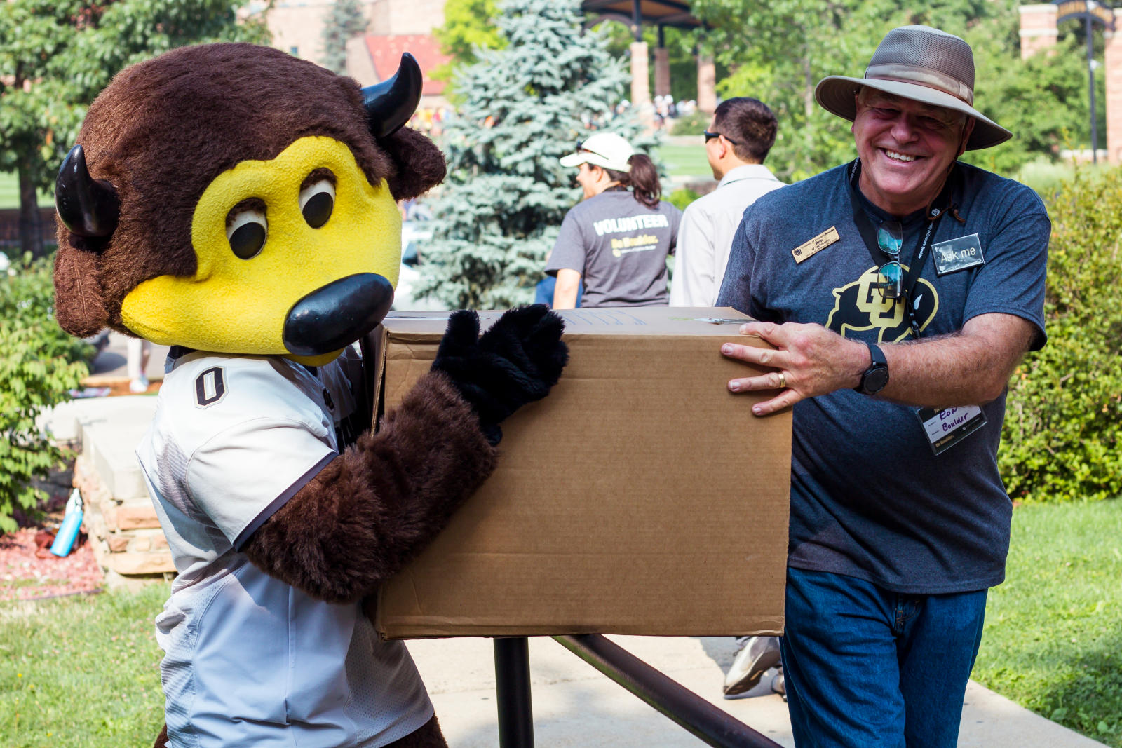 A person and Chip, the costumed mascot, carry a cardboard box together.