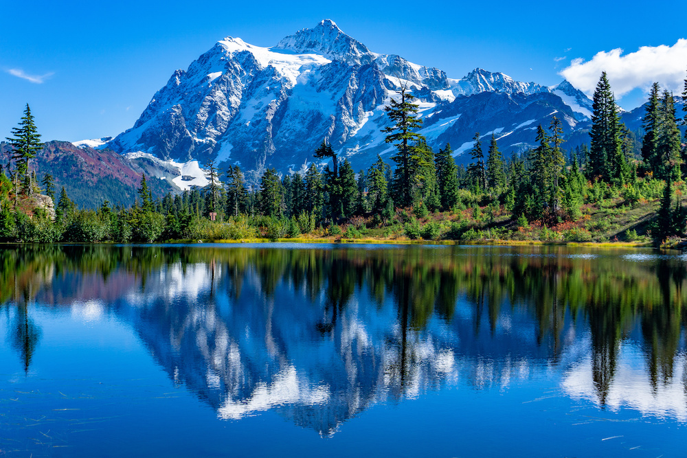 Snow-capped mountains and evergreens behind a glassy lake